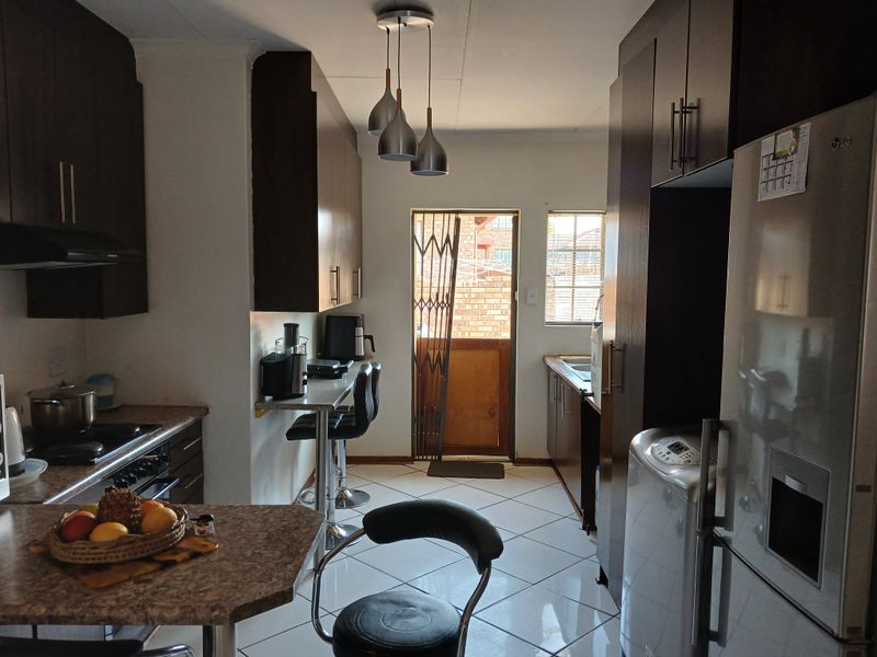 A functional kitchen featuring dark cabinetry, laminate countertops, tiled flooring, and direct access to the exterior via a security gate.
