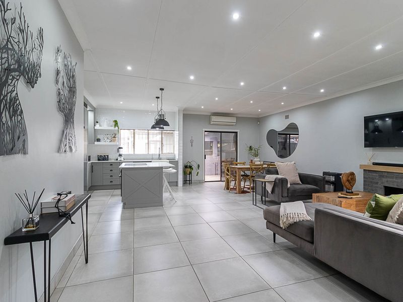 Spacious open-plan living area featuring a modern kitchen with island, tiled flooring, recessed lighting, and a stone-clad fireplace, creating a seamless flow.