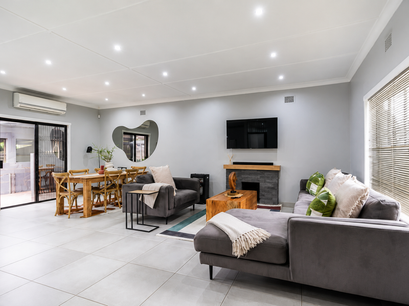 Spacious open-plan living and dining area featuring tiled floors, recessed lighting, a stone-clad fireplace, and direct access to an outdoor patio through sliding doors.