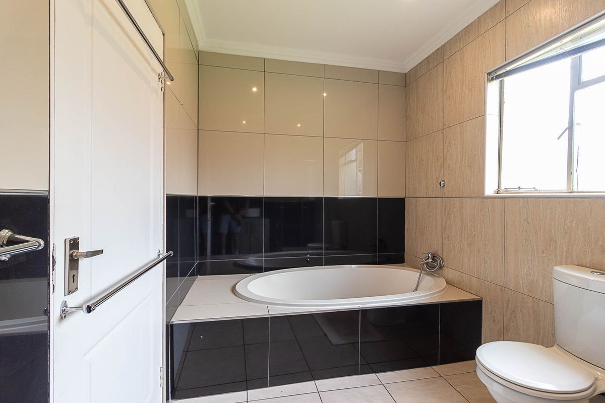 A clean, modern bathroom featuring a built-in oval bathtub, neutral-toned wall tiles, and a standard toilet.