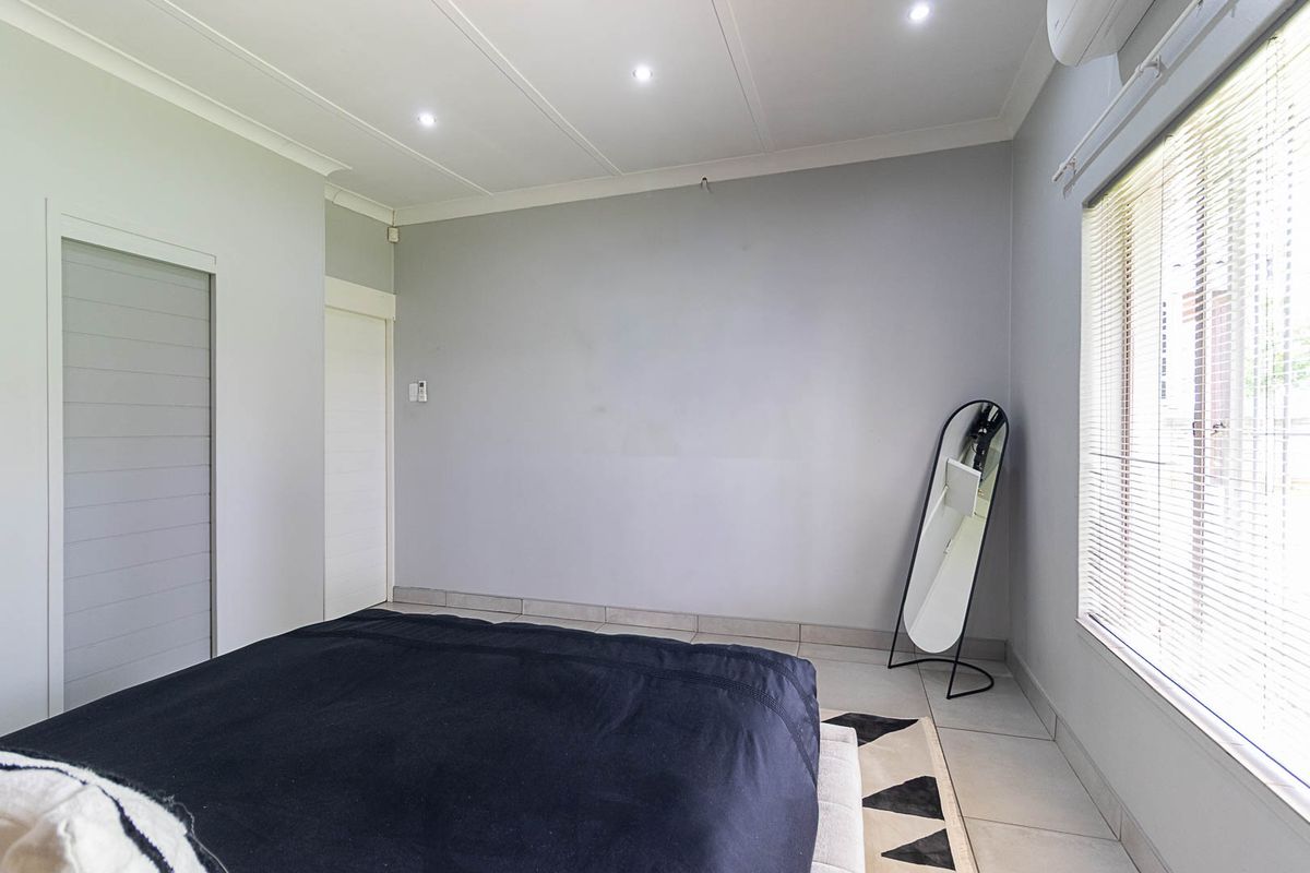 A bright bedroom featuring tiled flooring, recessed downlighting, coved ceilings, and venetian blinds, providing a clean and neutral foundation for living.