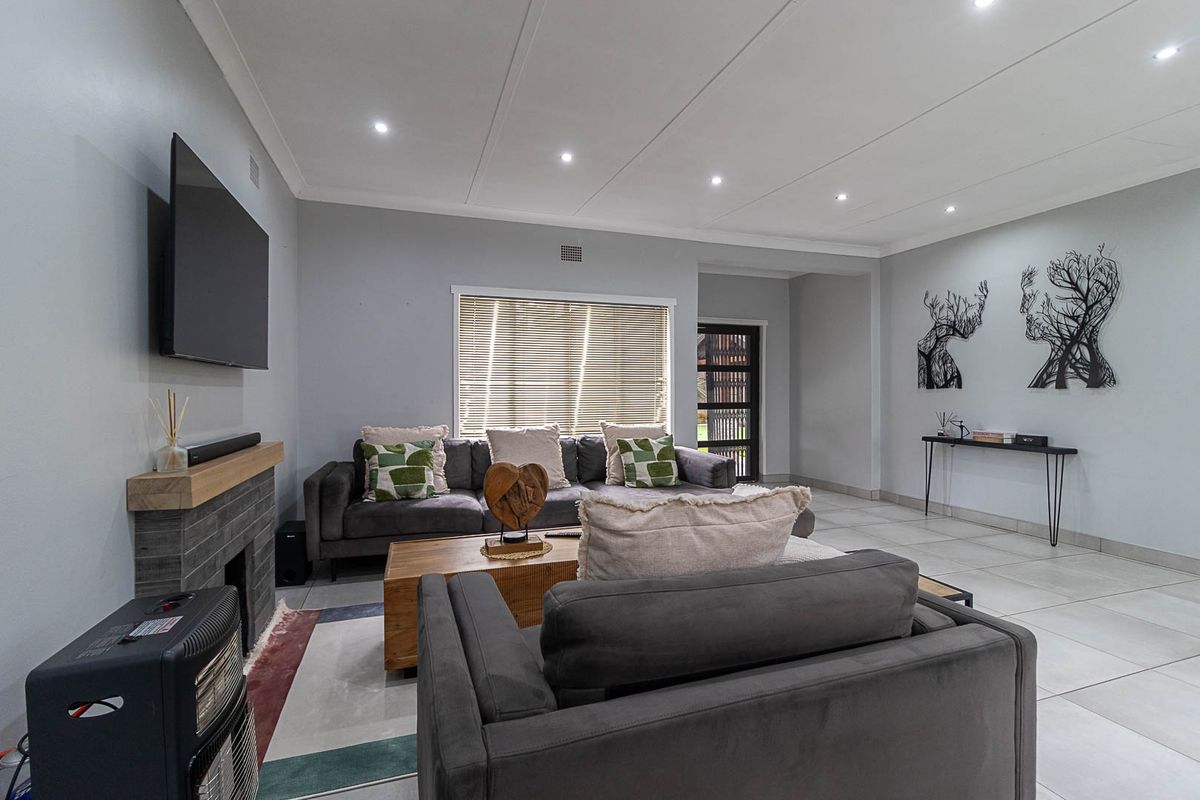 A well-maintained living room featuring tiled flooring, recessed downlights, and a modern fireplace with a timber mantelpiece.