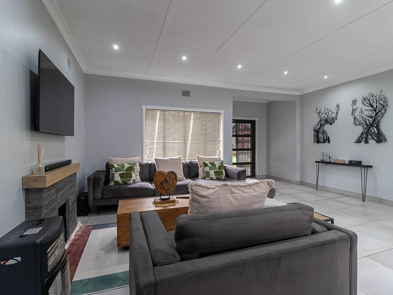 A well-maintained living room featuring tiled flooring, recessed downlights, and a modern fireplace with a timber mantelpiece.