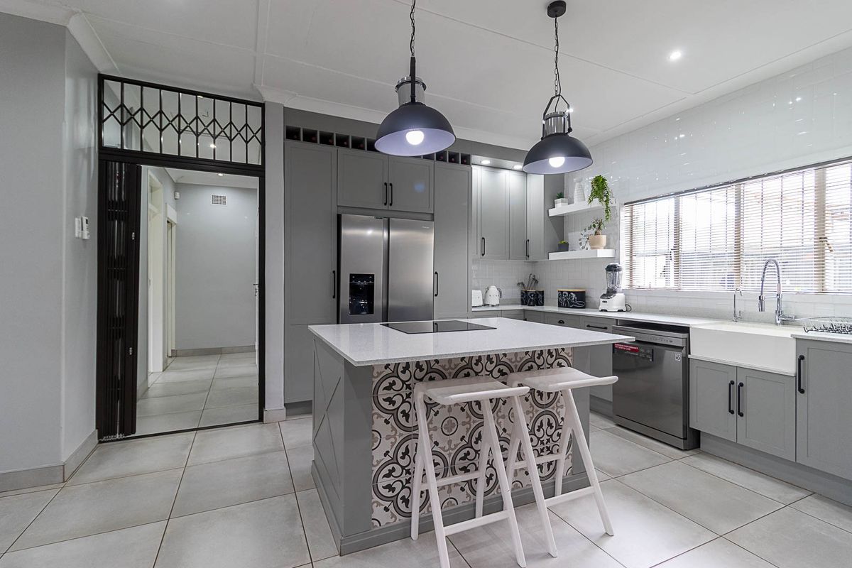 Modern kitchen featuring grey cabinetry, a central island with decorative tiling, quartz countertops, a farmhouse sink, and high-quality integrated appliances.
