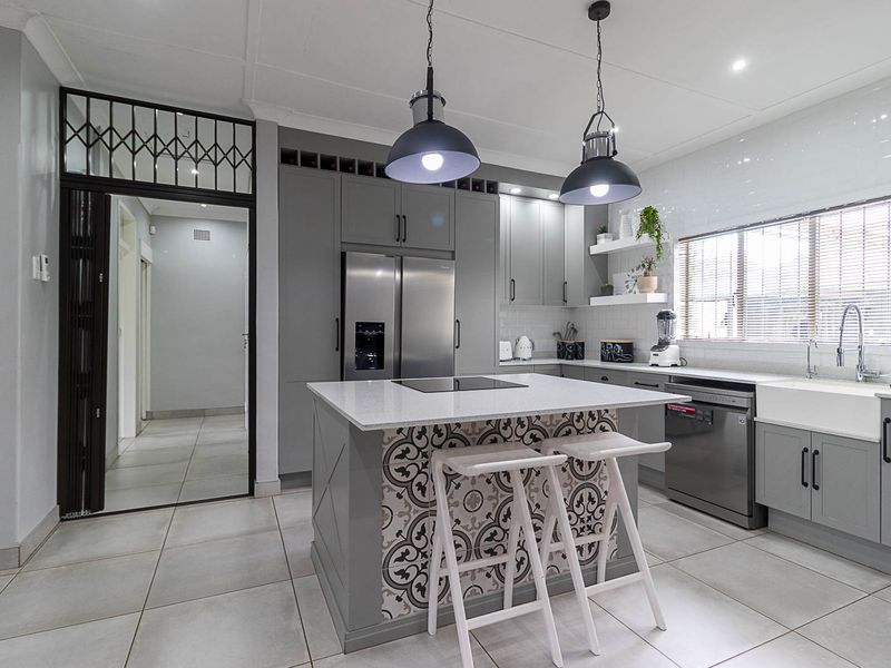 Modern kitchen featuring grey cabinetry, a central island with decorative tiling, quartz countertops, a farmhouse sink, and high-quality integrated appliances.