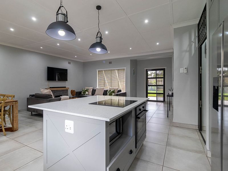 Modern open-plan living area featuring a central kitchen island with built-in appliances, tiled flooring, and a cozy fireplace, creating a seamless flow.