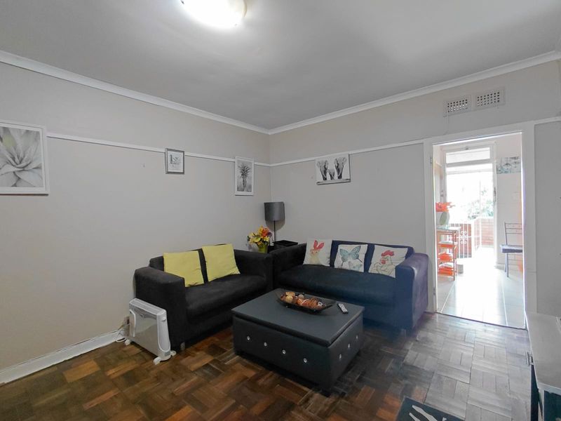A living room featuring classic parquet flooring, a picture rail, and a doorway leading to an adjacent outdoor area.
