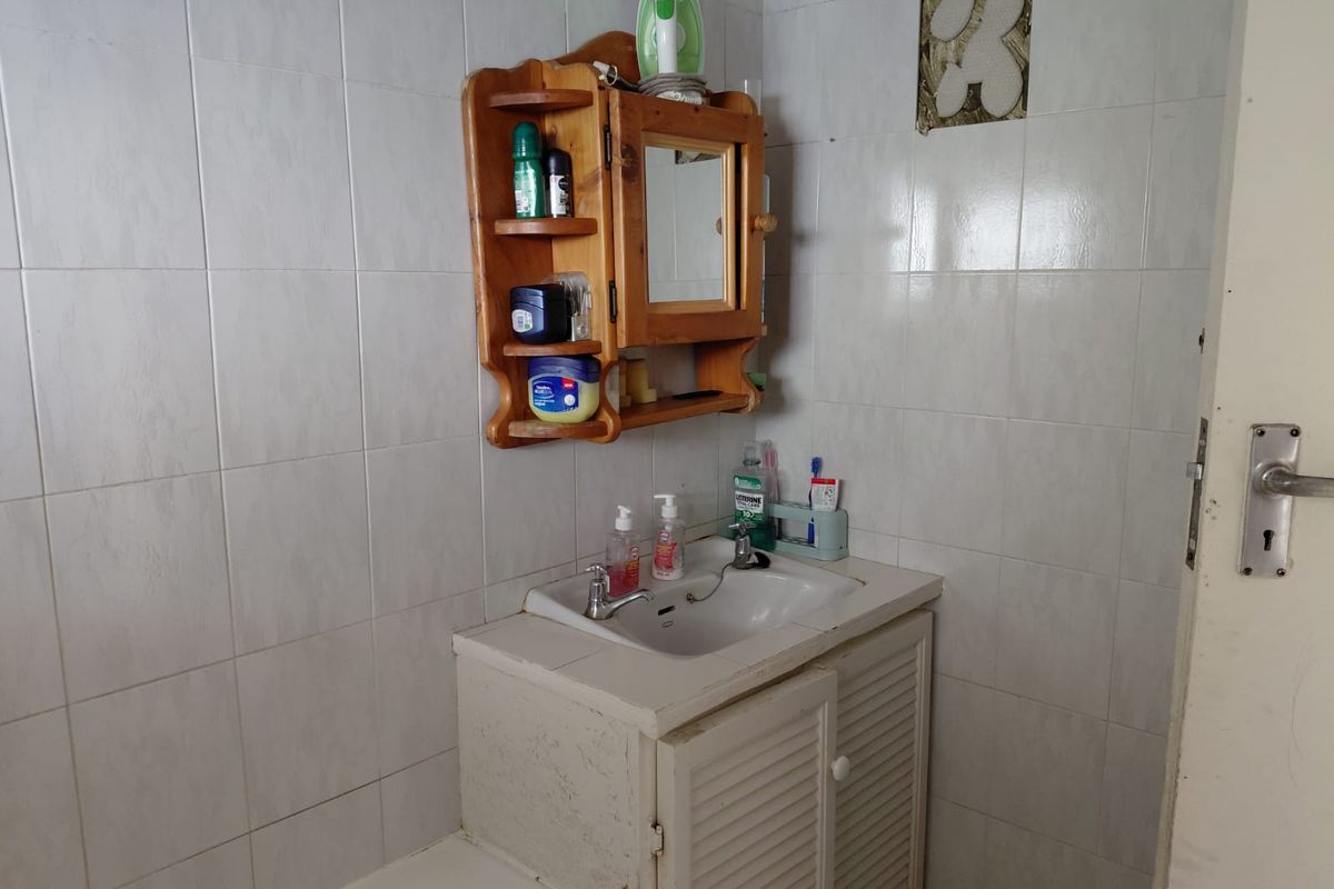 A bathroom featuring tiled walls, a built-in vanity cabinet with a washbasin, and a wall-mounted wooden medicine cabinet.