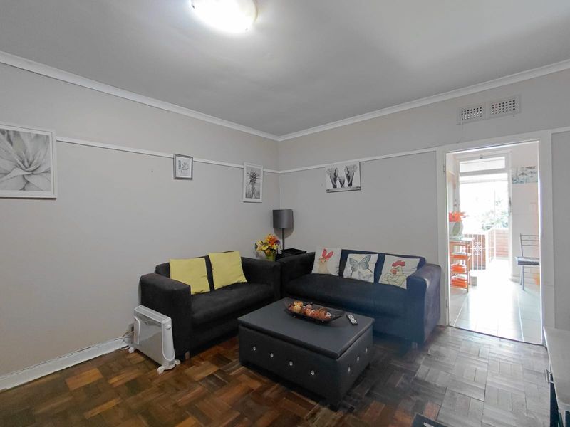 A living room featuring classic parquet flooring, ceiling cornicing, and a picture rail, with direct access to an adjoining balcony area.