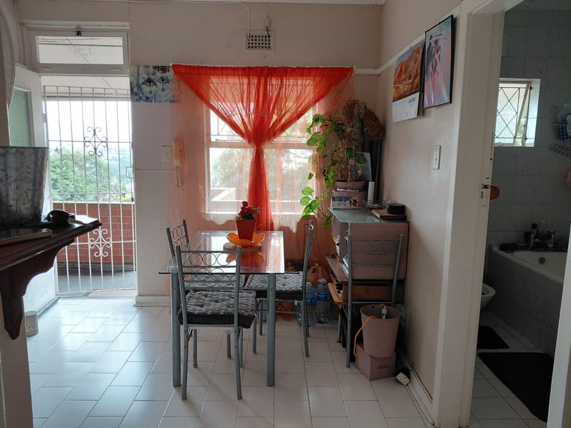 A compact dining area featuring tiled flooring and direct access to an outdoor balcony through a security gate.