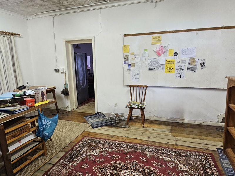 A living area featuring timber flooring and exposed ceiling beams, currently in need of cosmetic renovation and wall repairs.