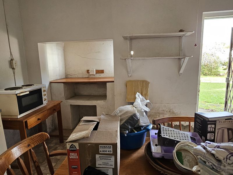 A dated kitchen area featuring a built-in masonry stove alcove, wall-mounted shelving, and direct access to the exterior via a security gate.