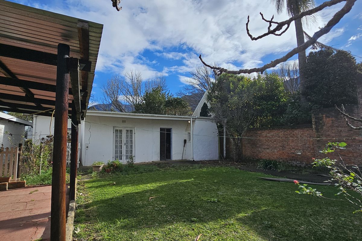 Rear view of the property featuring a covered patio area, a private lawn, and a brick boundary wall.