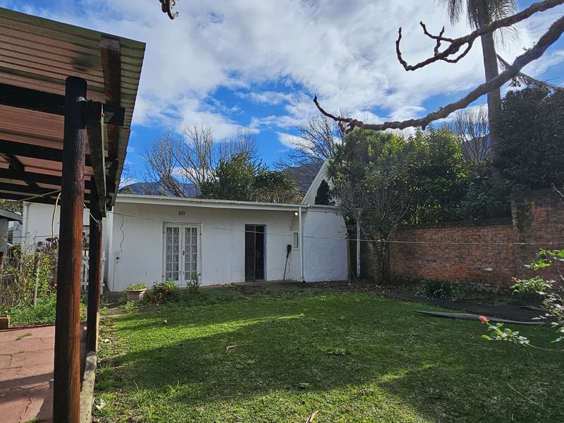 Rear view of the property featuring a covered patio area, a private lawn, and a brick boundary wall.