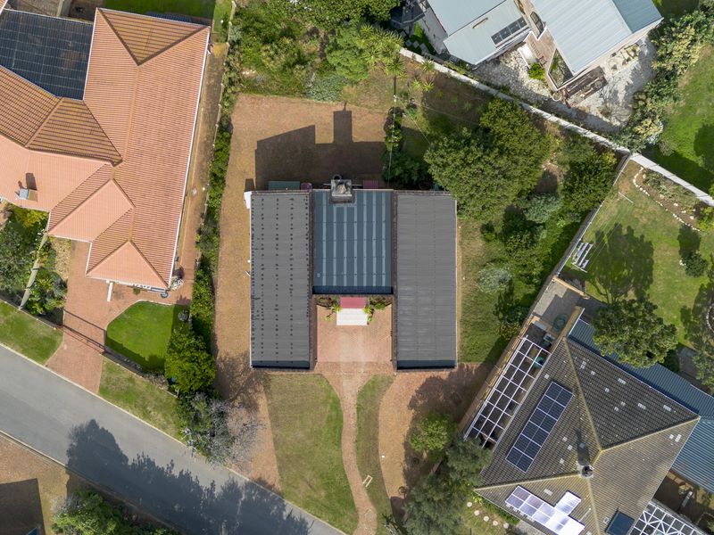 An aerial view of the property showing the building footprint, roof structure, surrounding garden, and driveway access within the residential estate.
