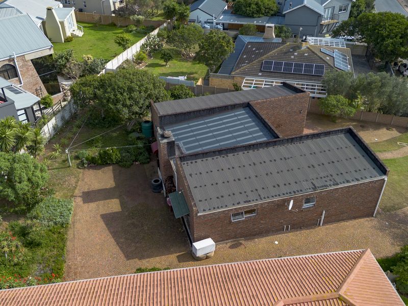 Aerial view of a brick house featuring a corrugated metal roof, paved driveway, and surrounding garden area within a residential neighborhood.