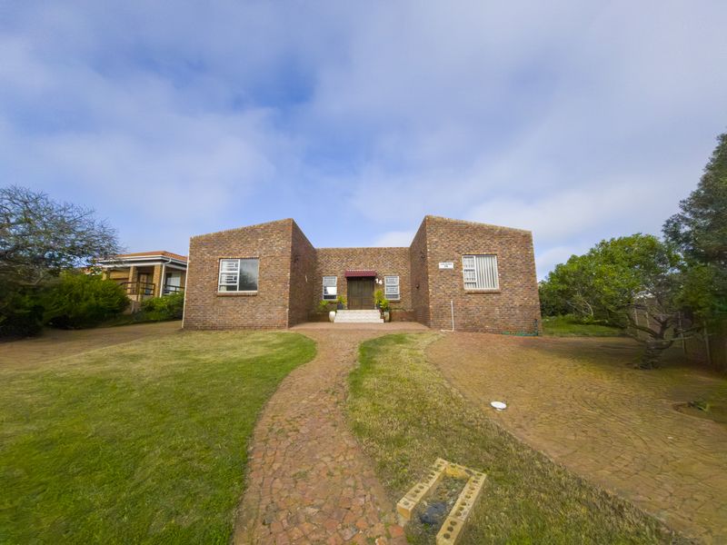 Front elevation of a face brick house featuring a paved driveway, central entrance with an awning, and established garden surroundings.