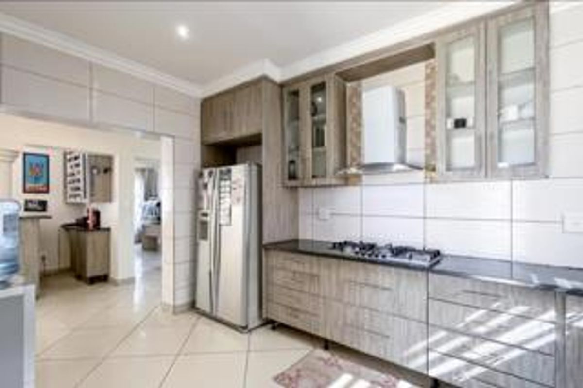 Modern kitchen featuring wood-finish cabinetry, granite countertops, a gas hob with extractor fan, and tiled flooring, with an open flow to adjacent living areas.