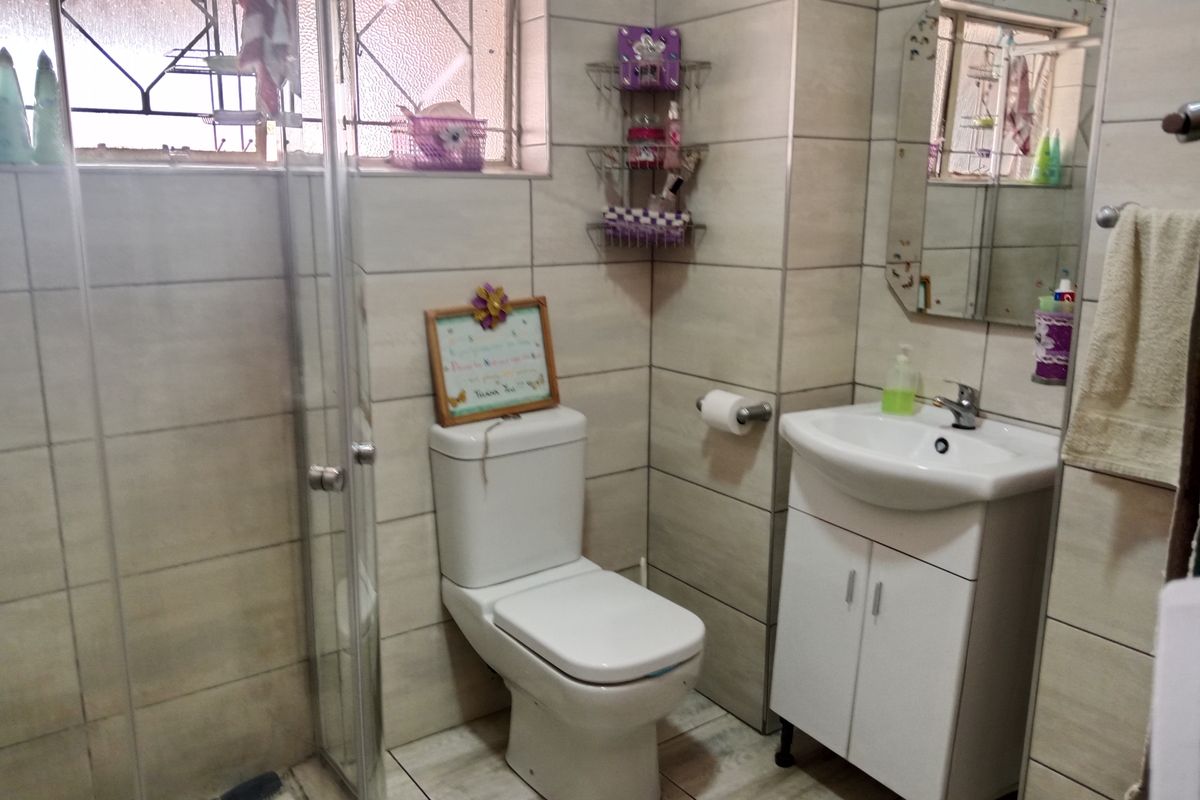 A functional bathroom featuring a shower enclosure, a modern vanity unit with a washbasin, and neutral wall and floor tiling.