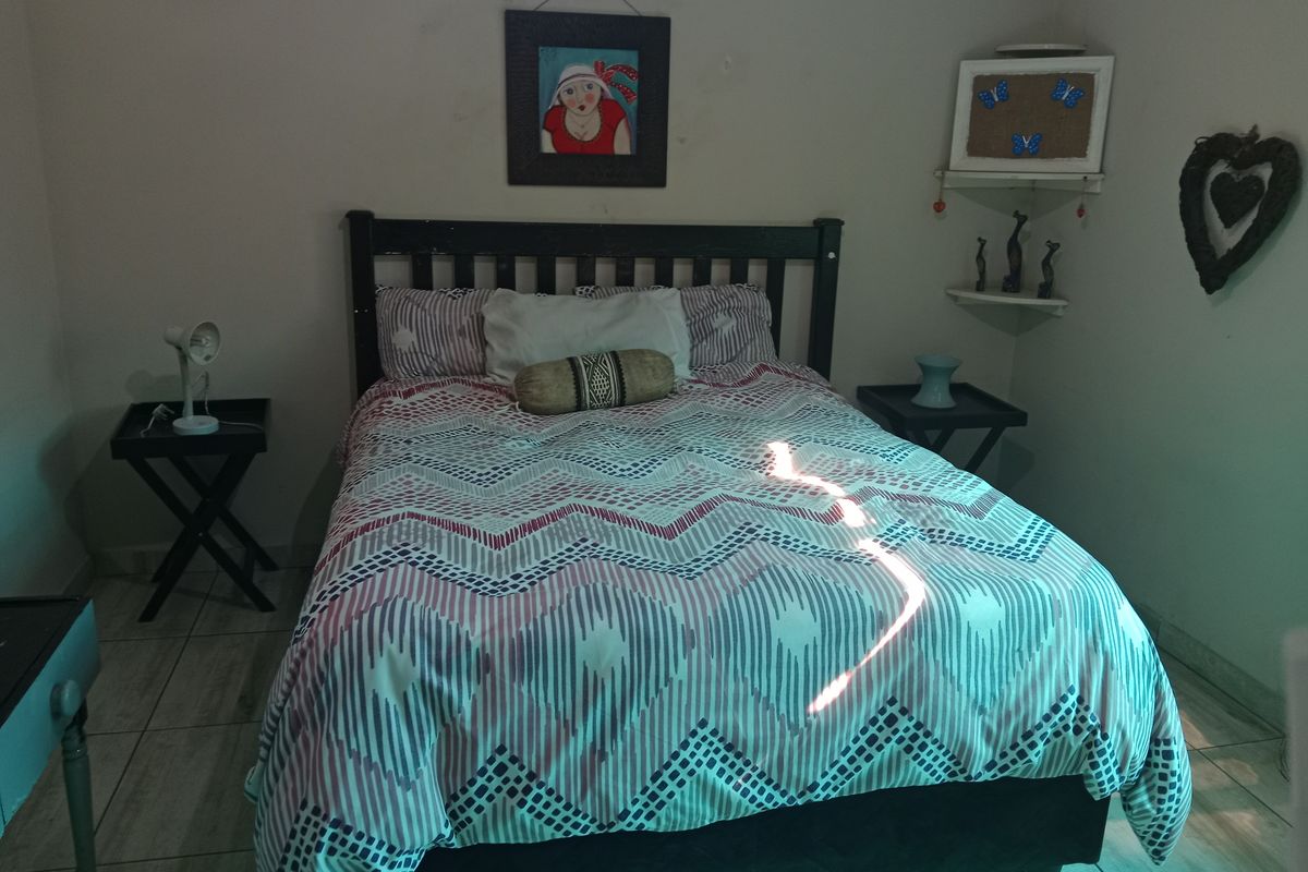 A bedroom featuring tiled flooring and corner shelving, currently furnished with a bed and side tables.