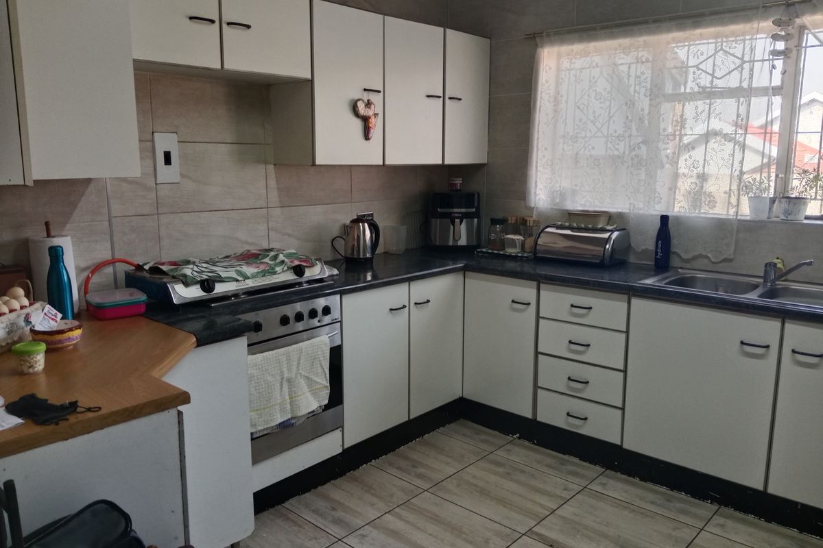 A functional kitchen featuring white cabinetry, dark laminate countertops, tiled backsplash, and a freestanding stove with a window providing natural light.