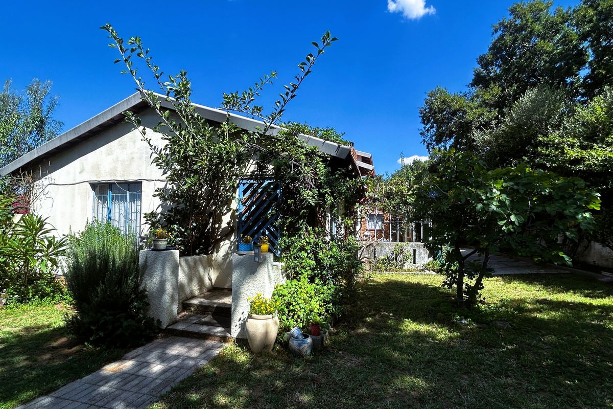 Rear exterior view of the house featuring a paved walkway, concrete steps, and established garden surroundings.