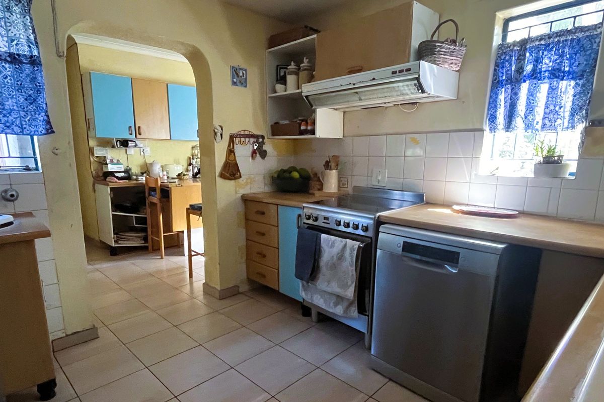 A dated kitchen featuring tiled flooring, wooden countertops, and built-in cabinetry, with an adjacent scullery area visible through the arched doorway.