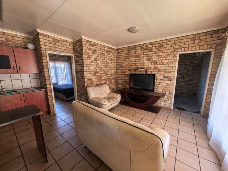 Open-plan living area featuring exposed brick walls and tiled flooring, seamlessly connected to a compact kitchen space.