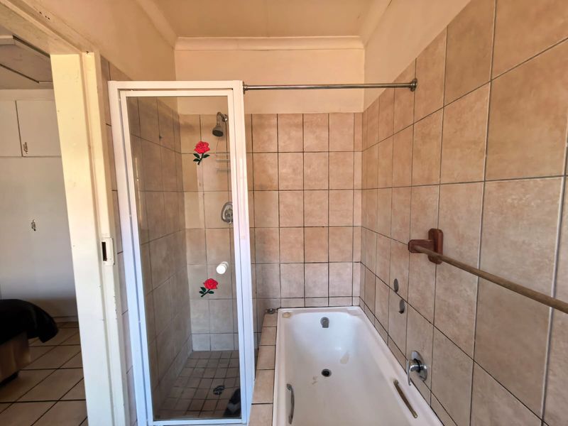 A dated bathroom featuring a combined shower and bathtub enclosure with neutral wall tiling and basic fixtures.