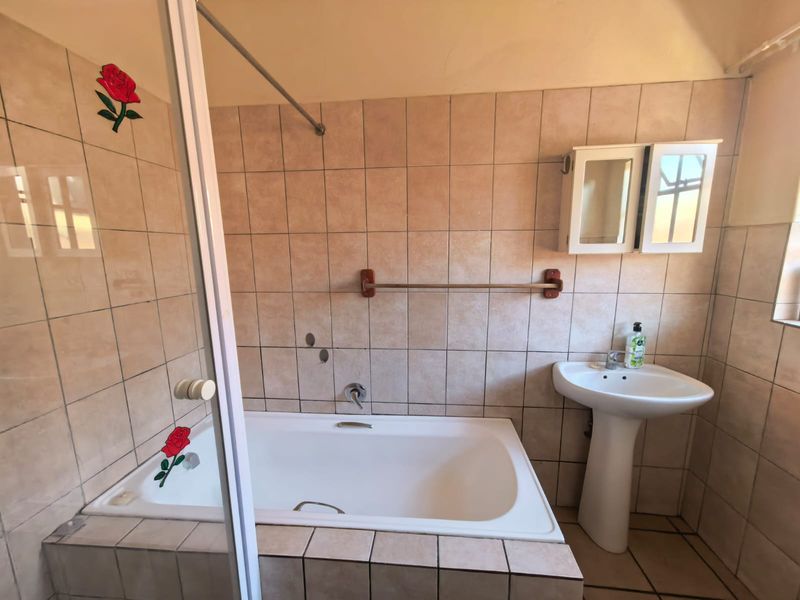 A dated bathroom featuring a built-in bathtub, pedestal basin, and wall-mounted medicine cabinet, finished with neutral wall and floor tiles.