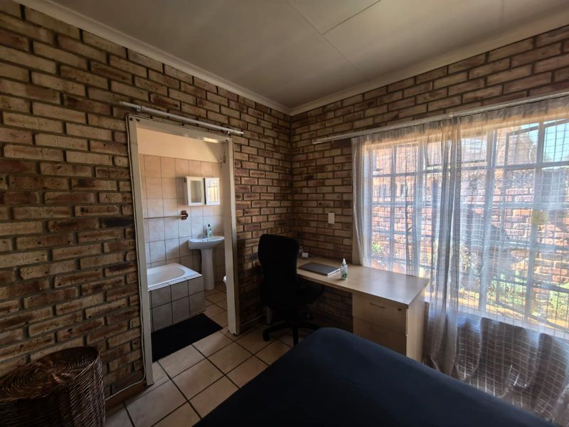 Bedroom featuring exposed brick walls, tiled flooring, and an en-suite bathroom with a bathtub and pedestal basin.