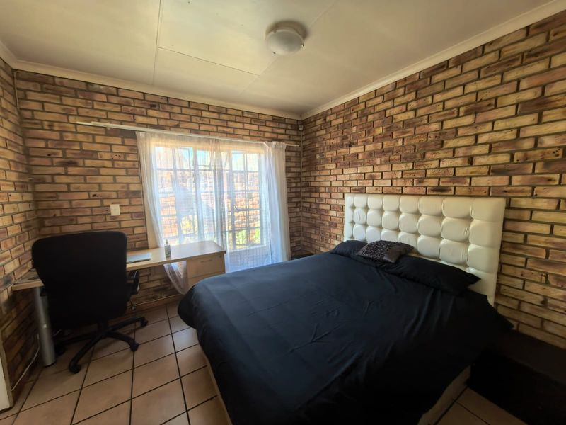 A bedroom featuring exposed brick walls, tiled flooring, and a ceiling-mounted light fixture, offering a rustic aesthetic with potential for modernization.