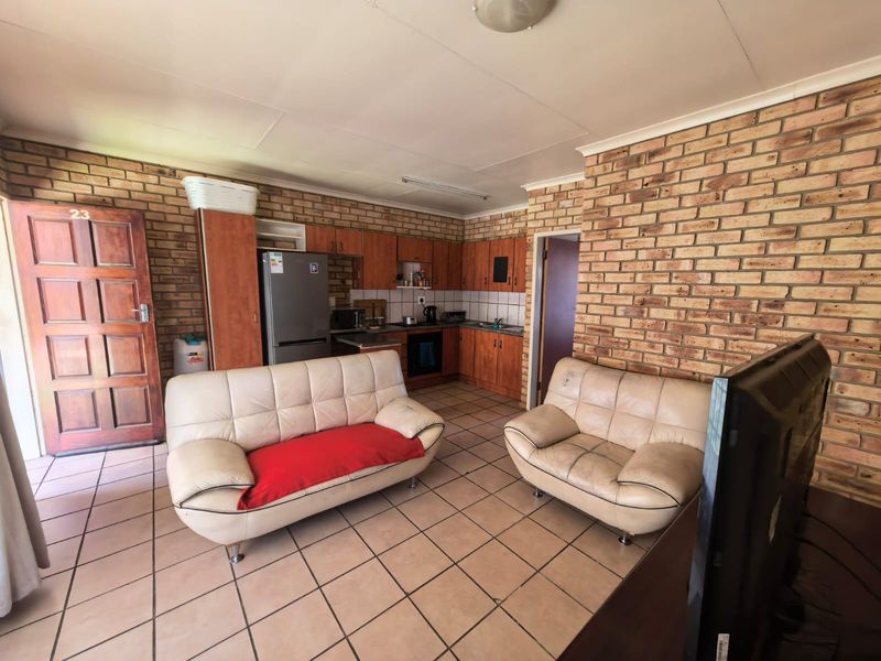 Open-plan living area featuring exposed brick walls, tiled flooring, and a functional kitchen with built-in cabinetry and appliances.