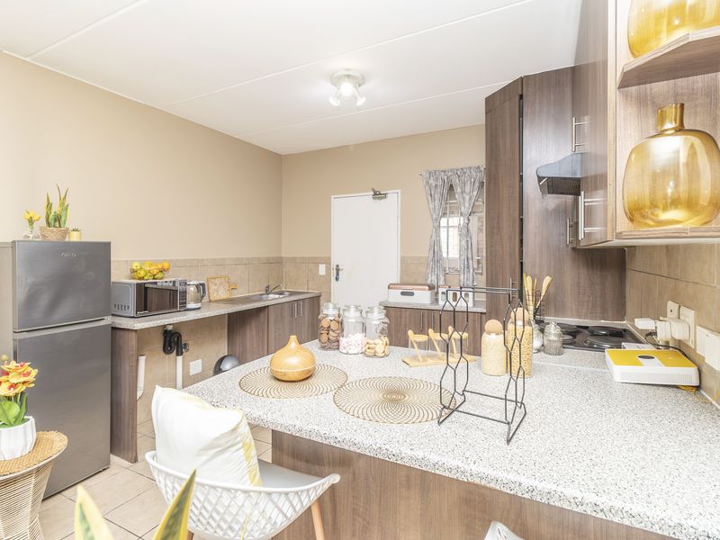 A functional kitchen featuring dark wood cabinetry, granite countertops, a gas hob with extractor fan, and a tiled backsplash.