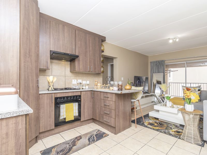 Open-plan kitchen and living area featuring wood-finish cabinetry, built-in appliances, tiled flooring, and direct access to a balcony through sliding glass doors.