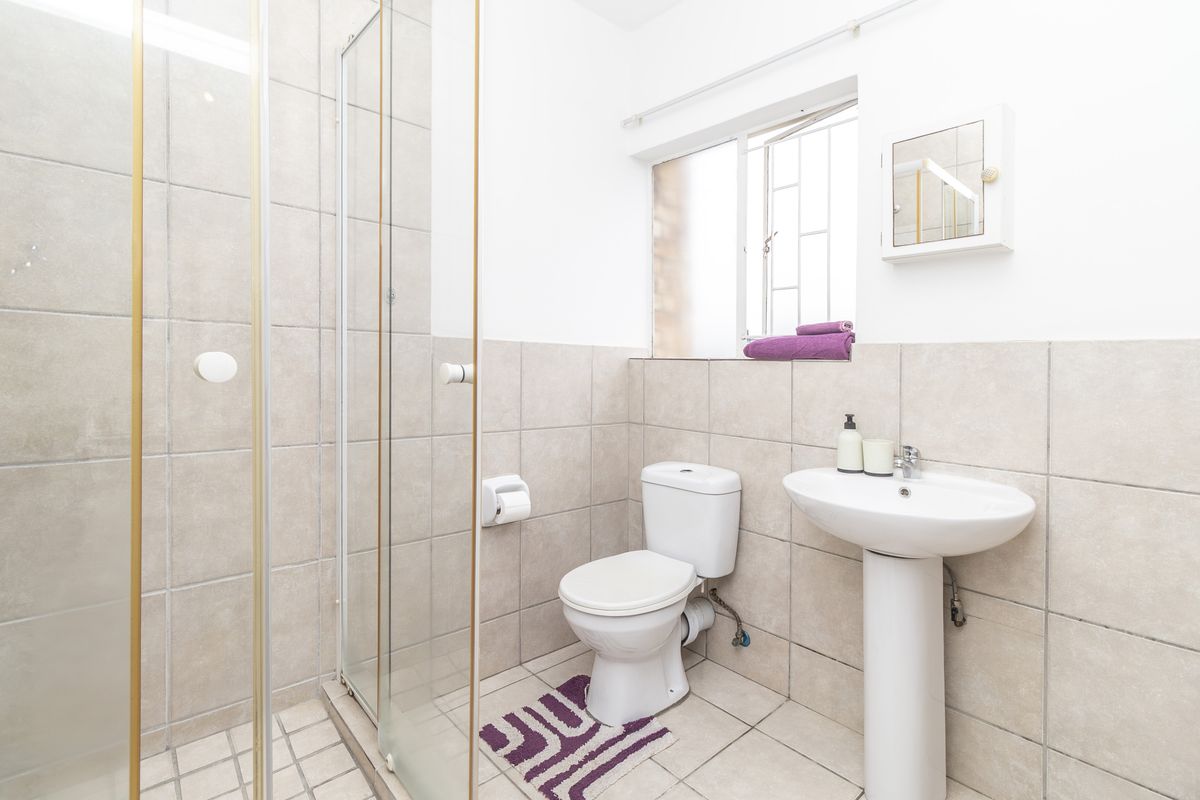 A functional bathroom featuring a pedestal basin, toilet, and a glass-enclosed shower with neutral wall and floor tiling.