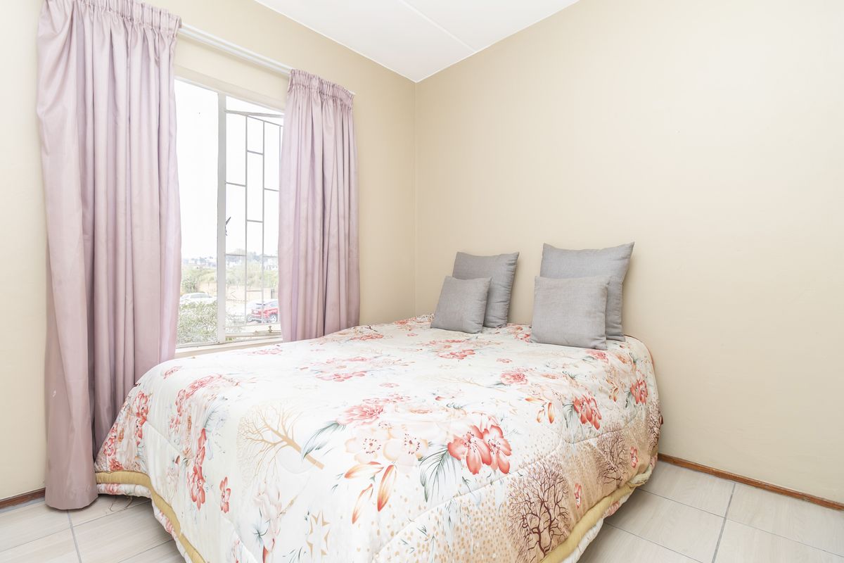 A functional bedroom featuring tiled flooring and a window fitted with security bars, providing natural light and ventilation.