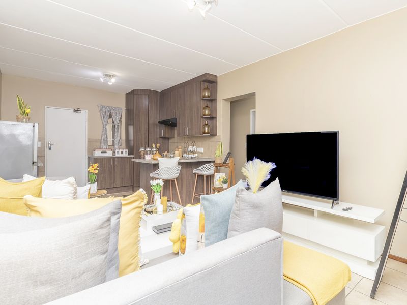 Open-plan living area featuring a compact kitchen with built-in cabinetry, a breakfast bar, and tiled flooring throughout the combined space.