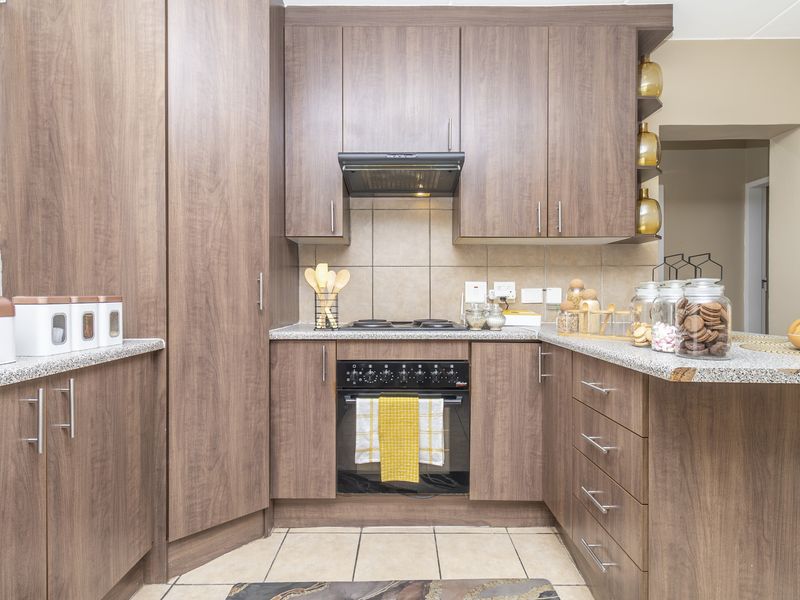 A functional kitchen featuring wood-finish cabinetry, granite countertops, a built-in electric oven and hob, and a tiled backsplash.