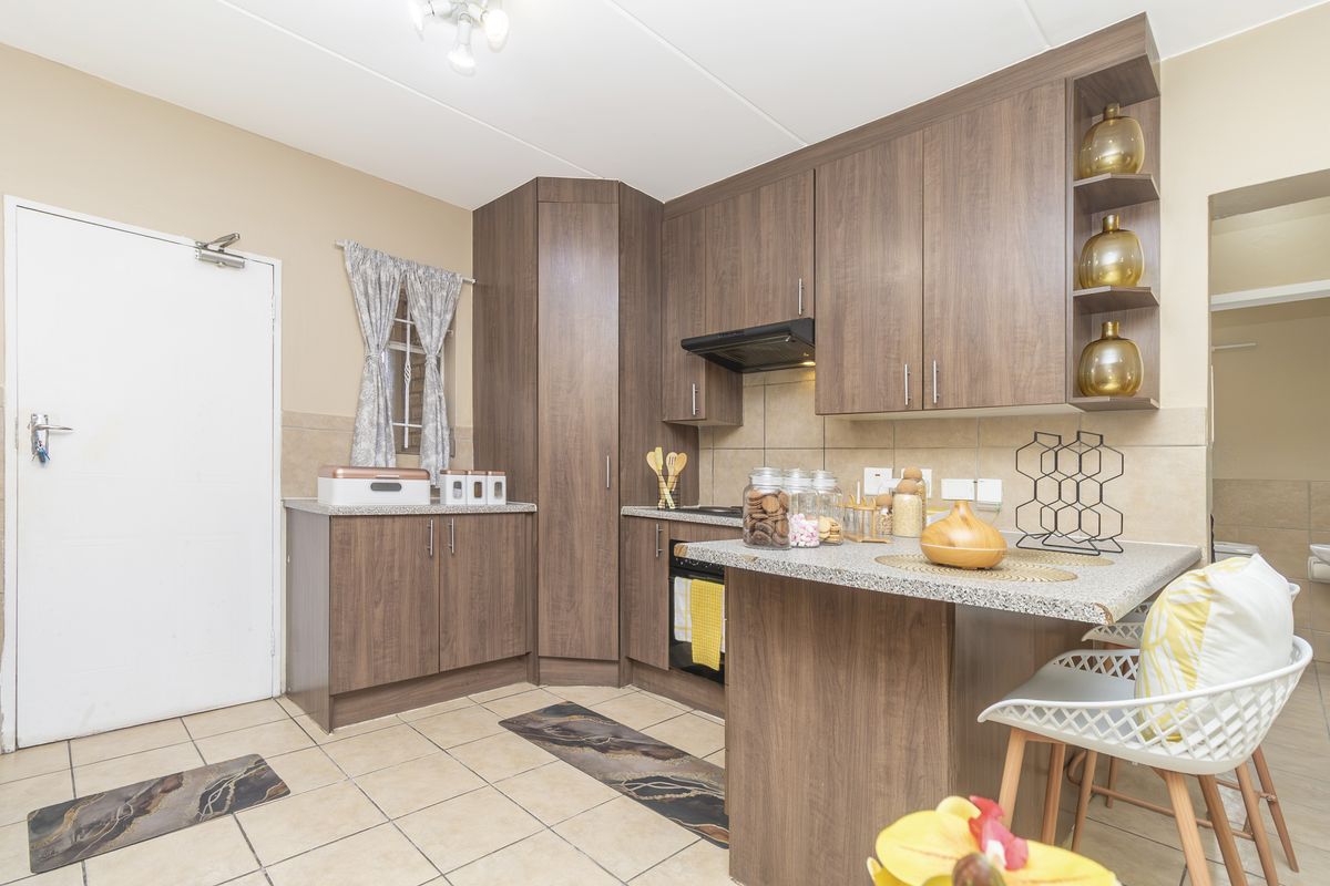 A functional kitchen featuring wood-look laminate cabinetry, granite countertops, built-in oven, extractor fan, and neutral ceramic floor tiling.