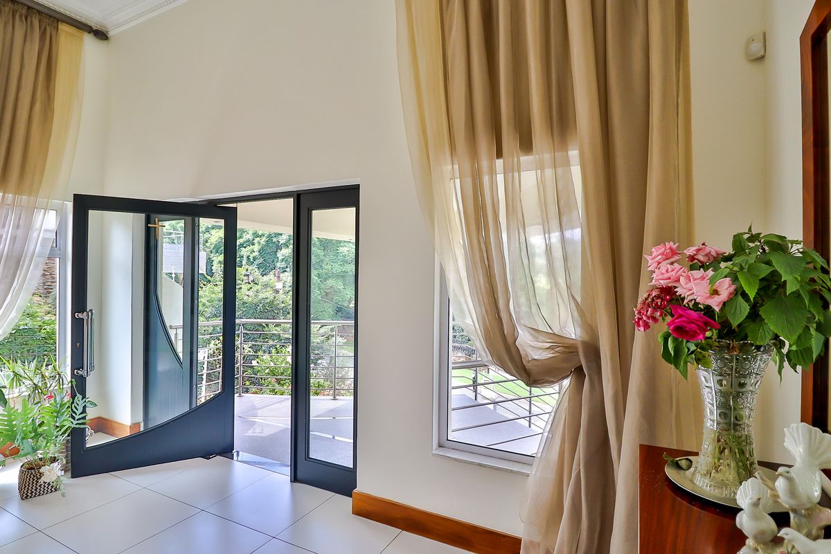 Bright living area featuring large aluminium-framed glass doors opening onto a balcony, complemented by neutral tiled flooring and elegant ceiling cornicing.