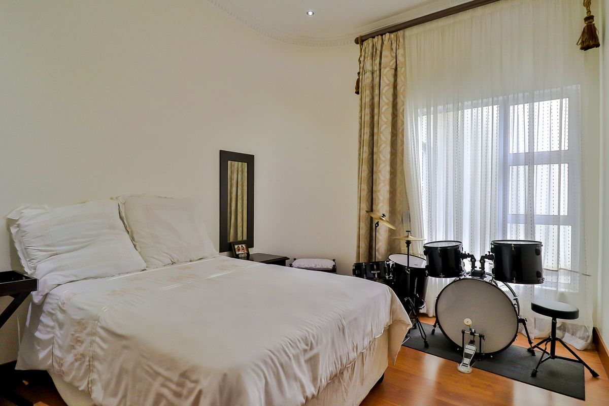 A well-lit bedroom featuring laminate flooring, coved ceiling details, and a large window with floor-to-ceiling curtains.