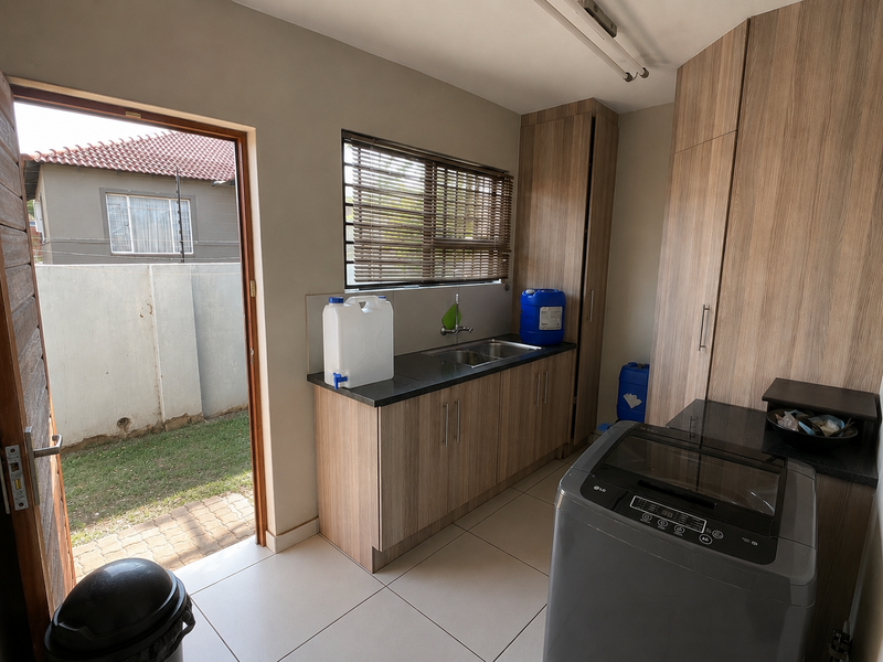 Functional laundry room featuring built-in wood-look cabinetry, double basin sink, tiled flooring, and direct access to the rear garden area.