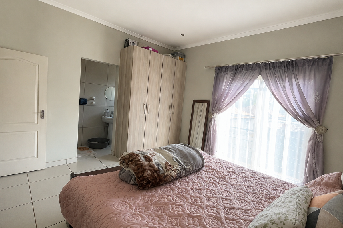 A well-maintained bedroom featuring tiled flooring, built-in wardrobes, and direct access to an en-suite bathroom, with natural light through large windows.