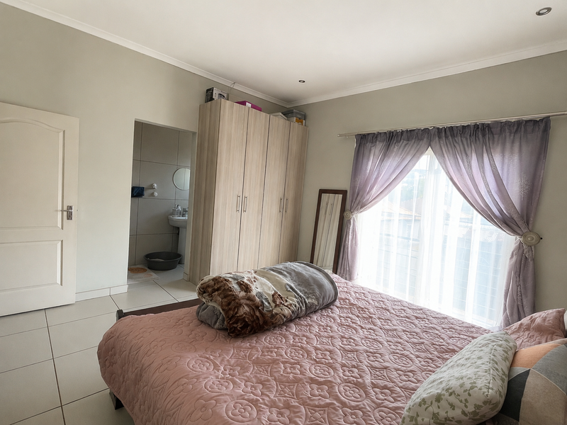 A well-maintained bedroom featuring tiled flooring, built-in wardrobes, and direct access to an en-suite bathroom, with natural light through large windows.