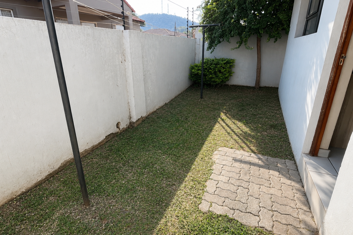 A private rear courtyard featuring a small lawn, paved area, and perimeter wall with electric fencing.