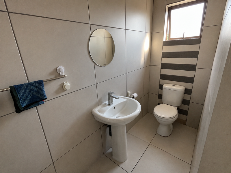 A clean and modern guest bathroom featuring a pedestal basin, toilet, and neutral floor-to-ceiling tiling with a decorative accent strip.