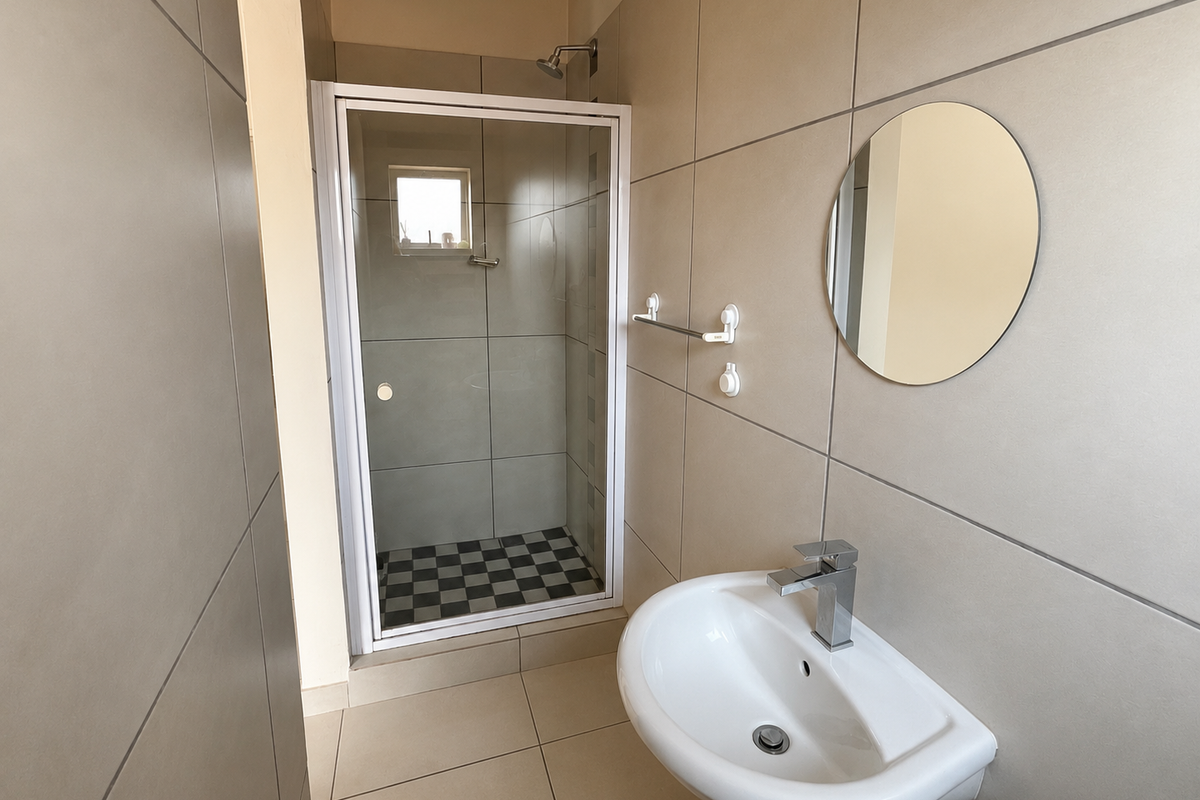 A clean, modern bathroom featuring a glass-enclosed shower, pedestal basin with mixer tap, and neutral large-format wall tiles.