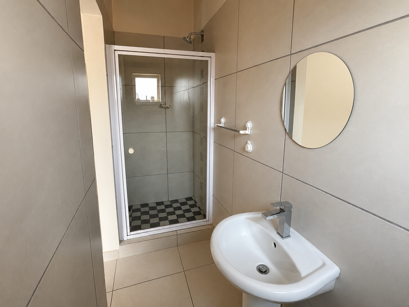 A clean, modern bathroom featuring a glass-enclosed shower, pedestal basin with mixer tap, and neutral large-format wall tiles.