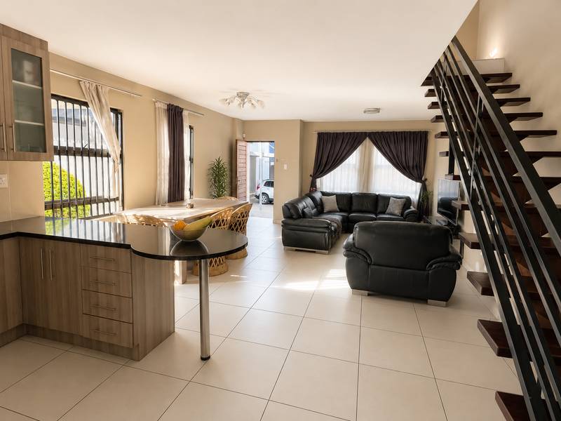 Spacious open-plan living area featuring a modern kitchen with granite countertops, tiled flooring, and a contemporary staircase leading to the upper level.